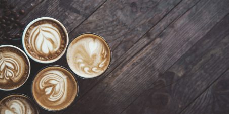 photo of 5 coffee cups in a row, on a wooden table, decorated with a froth art.