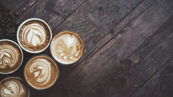 photo of 5 coffee cups in a row, on a wooden table, decorated with a froth art.